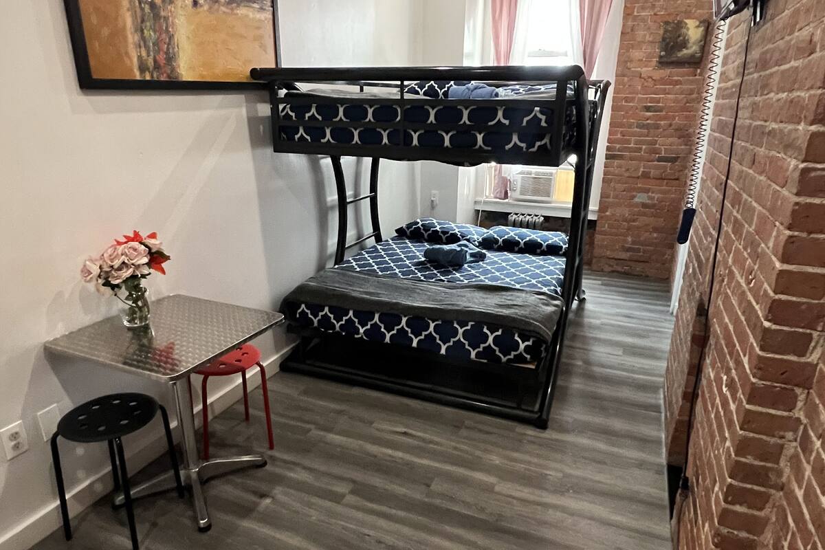 Habitación con literas, un escritorio y silla, un florero con flores y un cuadro en la pared.