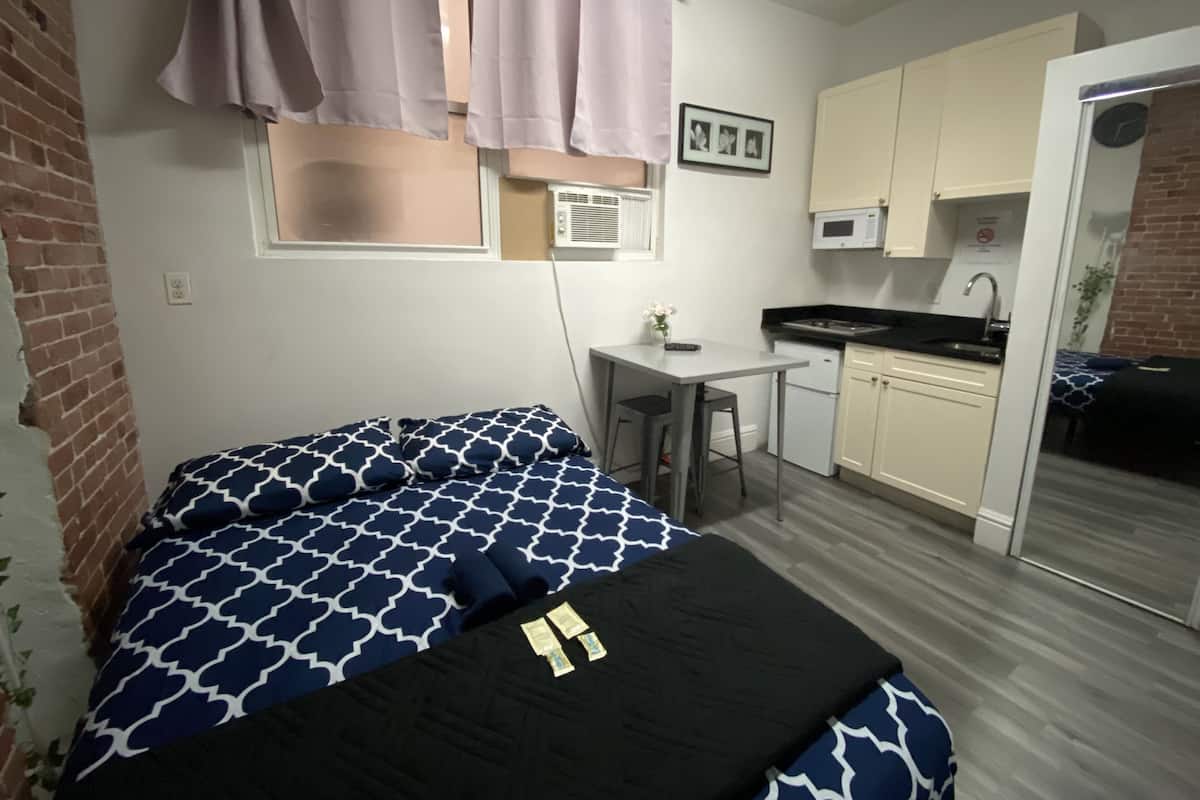 Una habitación pequeña con cama, kitchenette y baño.