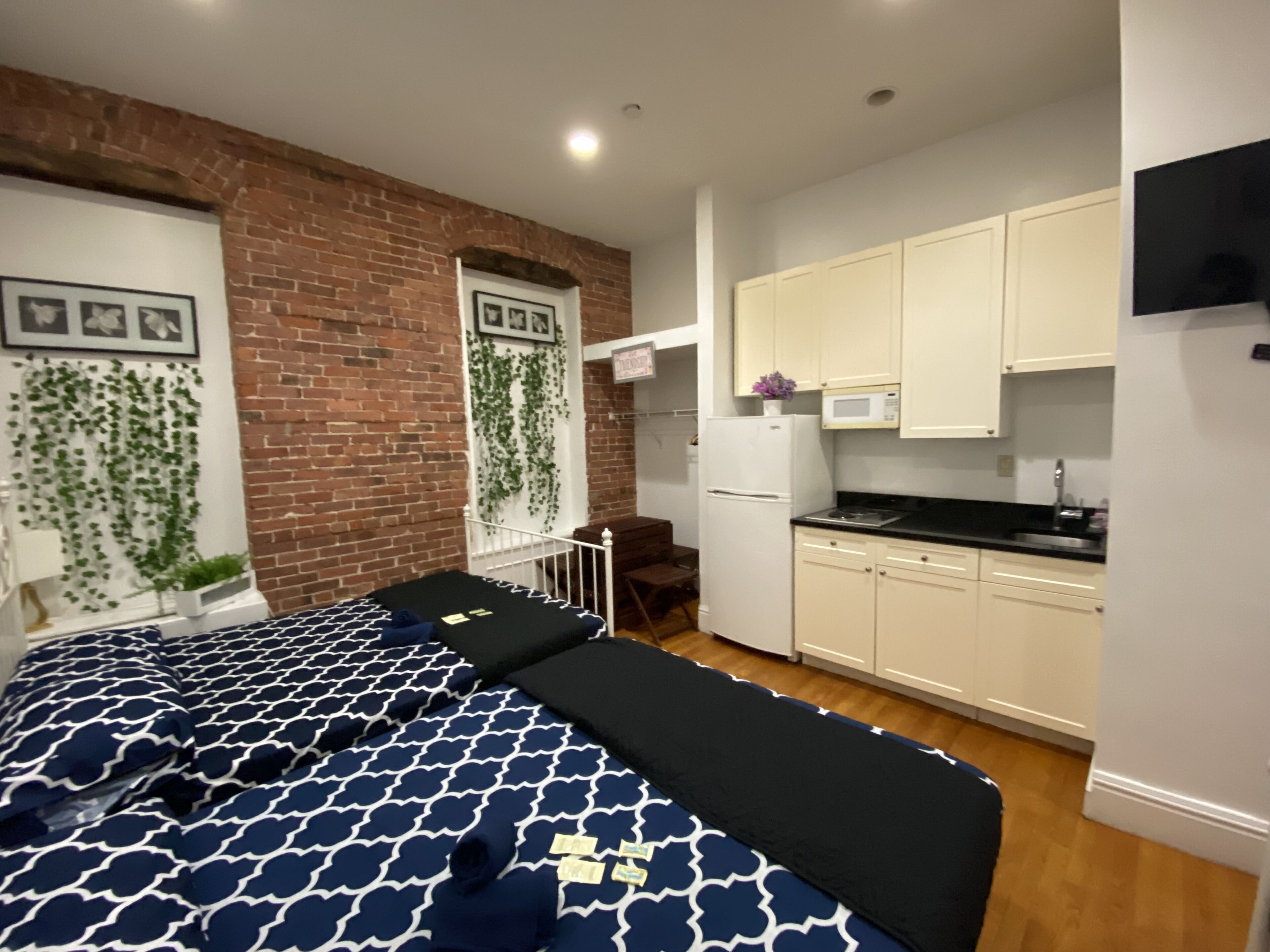 A compact room with a bed, a small kitchenette, and a brick wall.