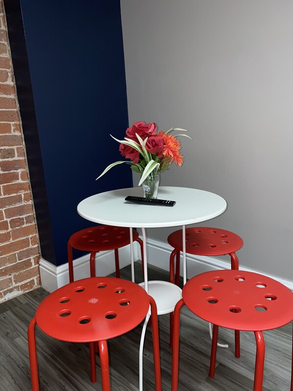A small dining area with a white table and four red chairs, a vase with flowers, and a remote control on the table.