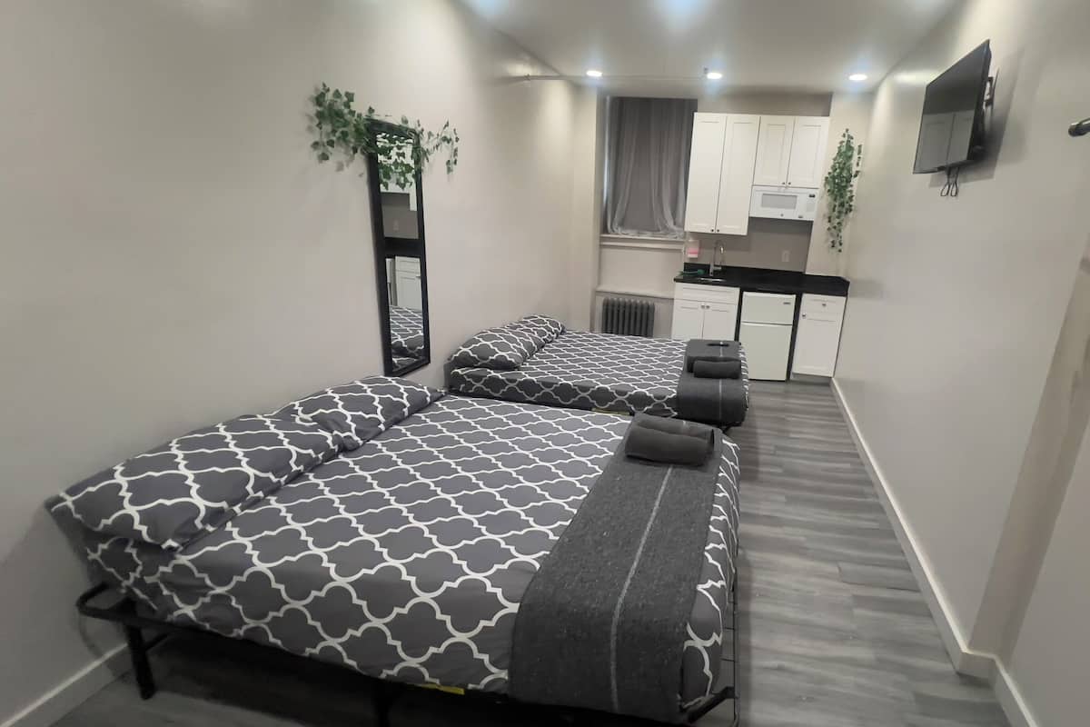 Una habitación de hotel compacta con dos camas, un kitchenette, un televisor y un espejo.