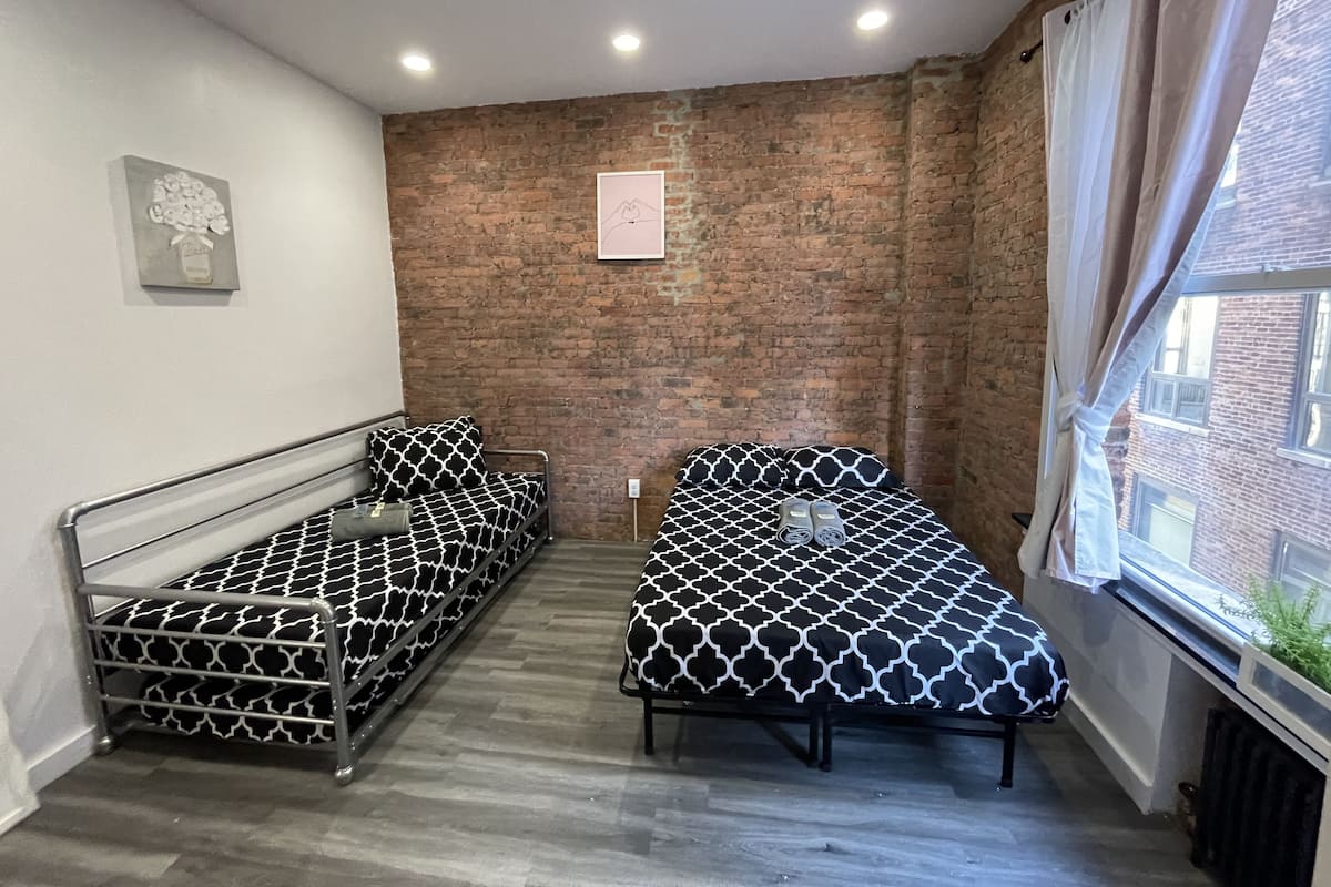 Una habitación con dos camas, una pared de ladrillo, una ventana con cortinas y un radiador.