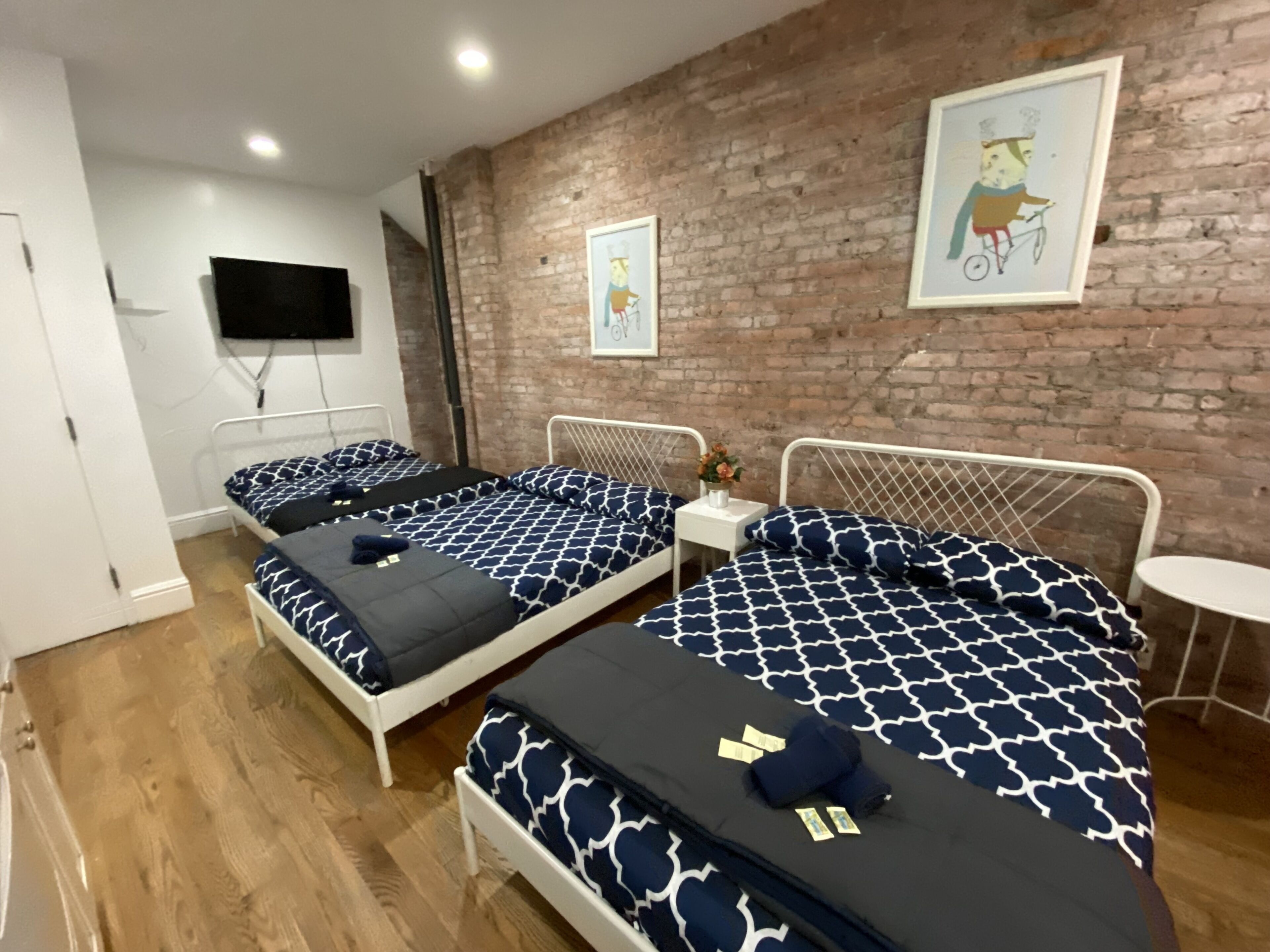 Une chambre d’hôtel avec deux lits, un mur en briques, une petite table et un téléviseur fixé au mur.