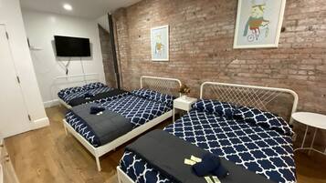 A hotel room with two beds, a brick wall, a small table, and a mounted TV.