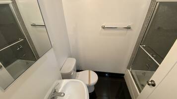 A small, modern bathroom with a white toilet, a sink, and a glass shower enclosure.