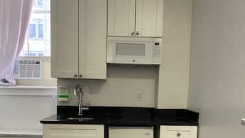 A compact kitchen with white cabinets, a black countertop, a built-in microwave, and a refrigerator.