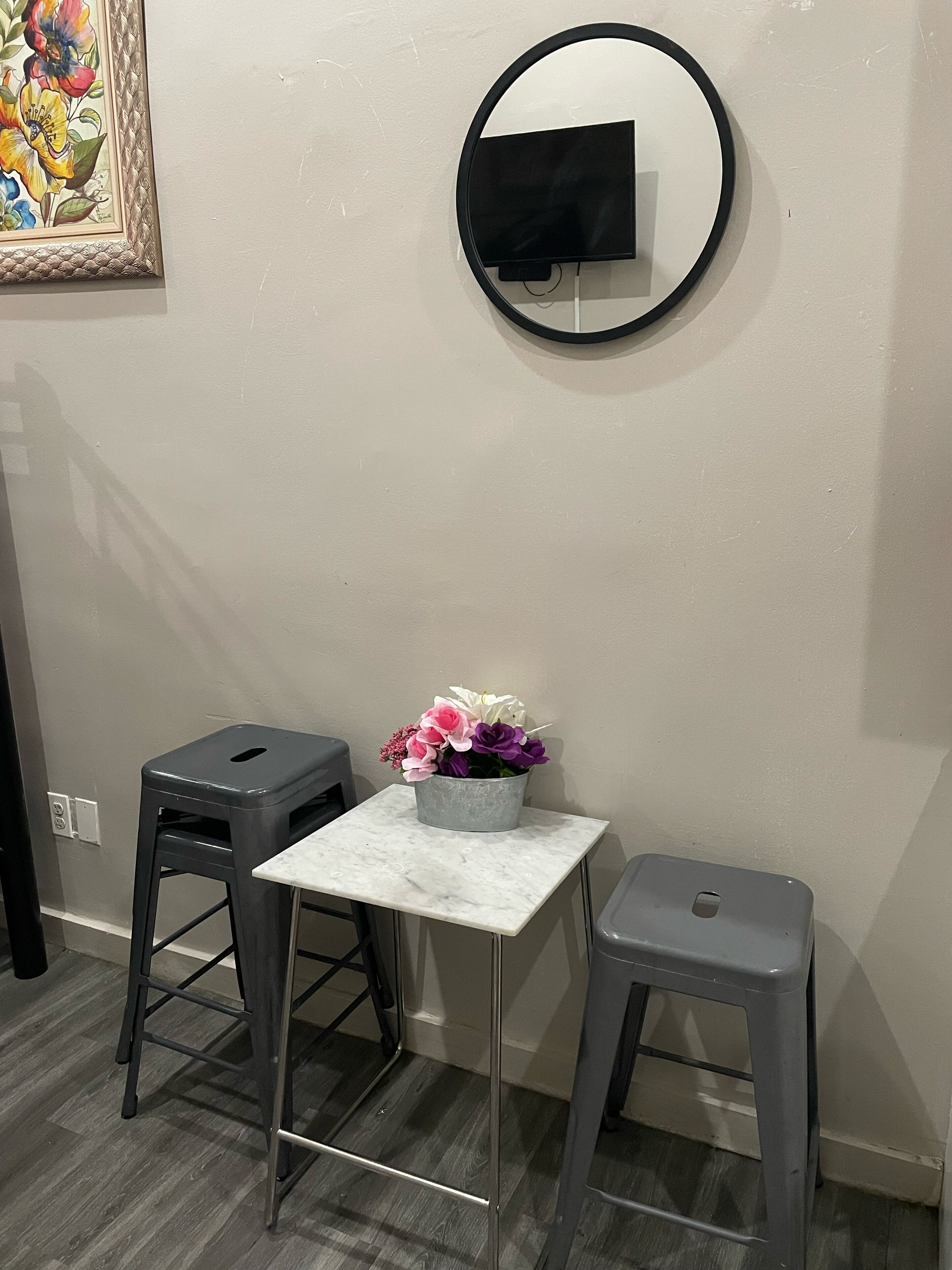 A small room with a round mirror, a white table, and two grey stools.