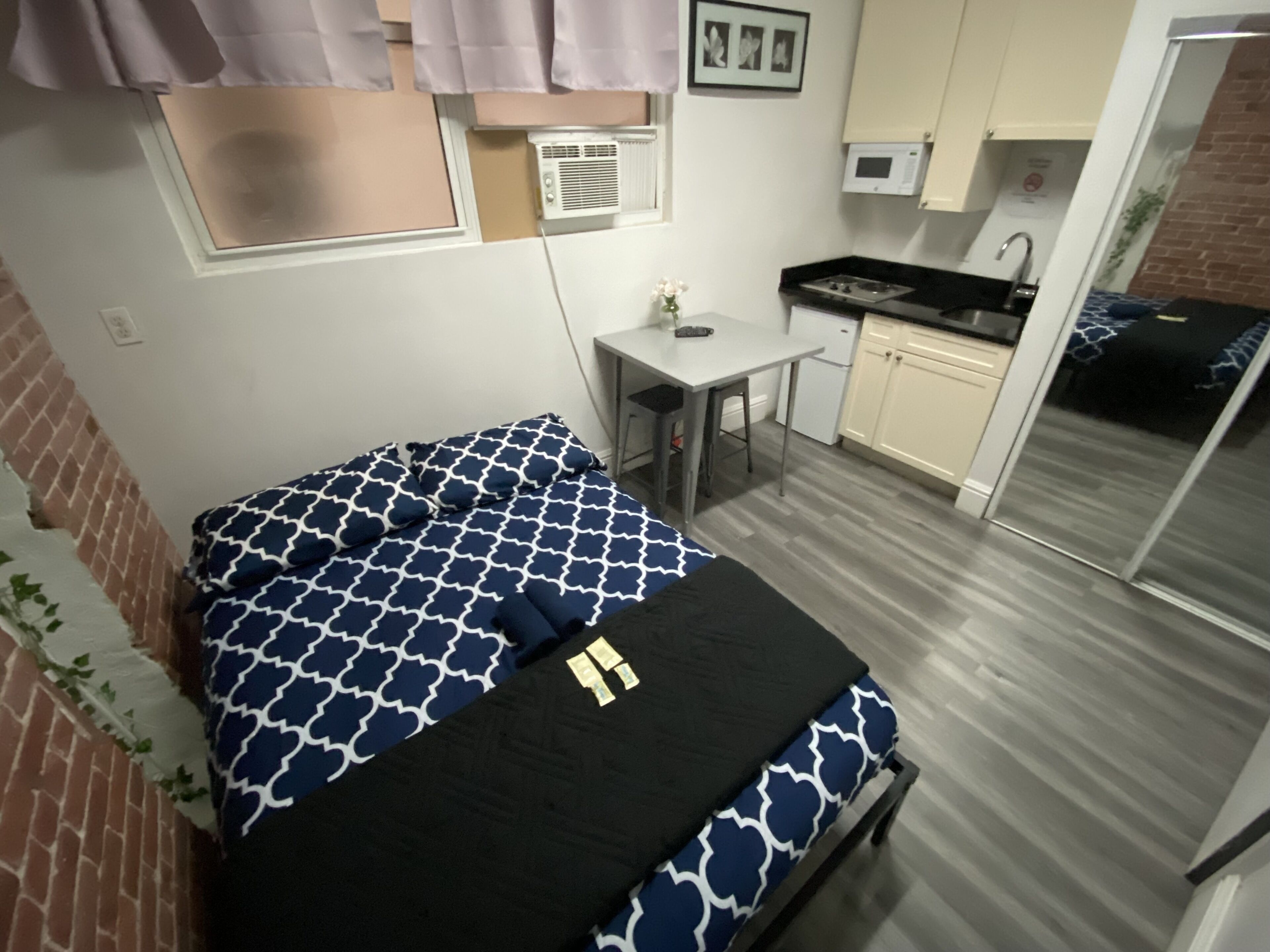 Een compacte kamer met een bed, een klein tafeltje, een kitchenette en een schuifdeur naar een balkon.