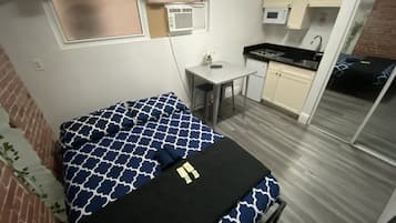 Een compacte kamer met een bed, een klein tafeltje, een kitchenette en een schuifdeur naar een balkon.