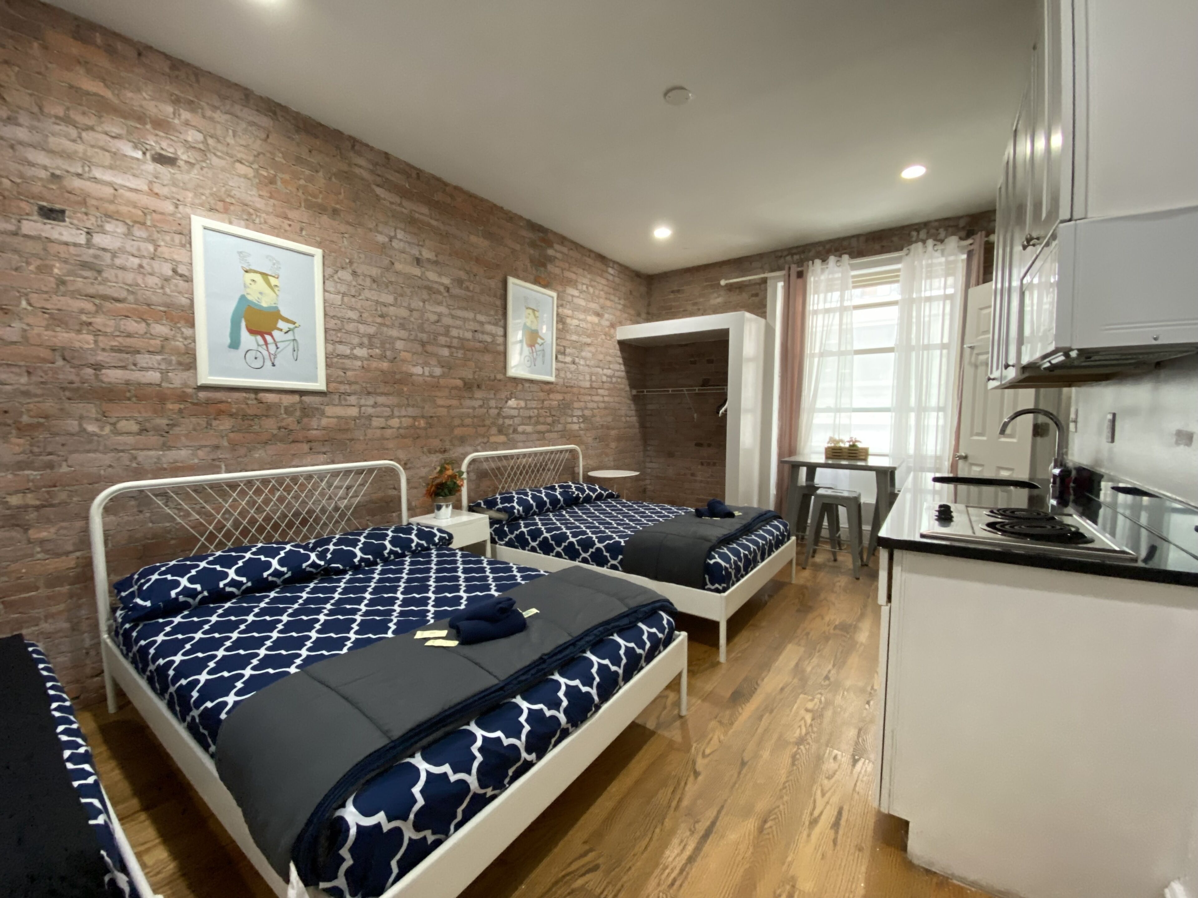 Une chambre avec deux lits, un coin cuisine et un mur en briques.