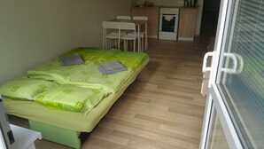 A small, neatly arranged bedroom with a single bed, a desk, and a kitchenette.