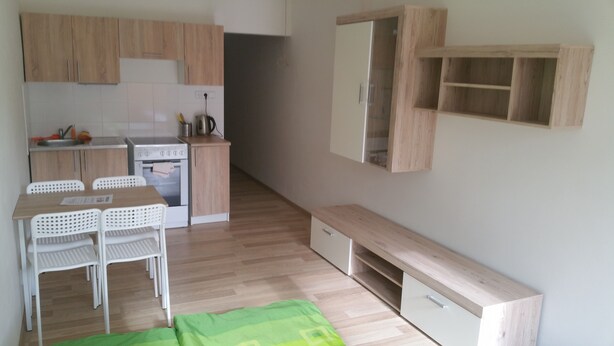 A compact kitchen with wooden cabinets, a stove, and a dining area with chairs.