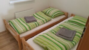 Un alojamiento pequeño, una habitación individual con dos literas de madera, cada una con ropa de cama y almohadas a rayas verdes y blancas a juego.