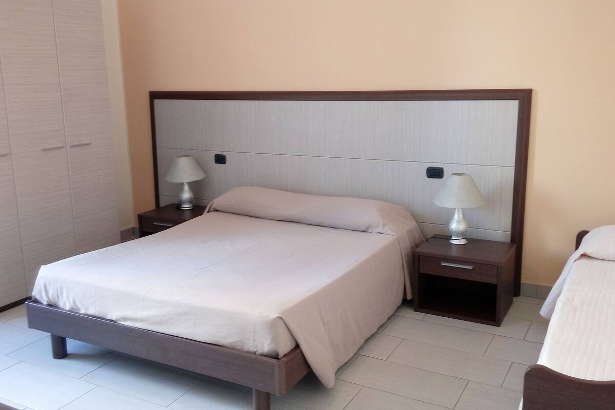 A hotel room with a bed, two bedside tables with lamps, a wardrobe, and a chair.
