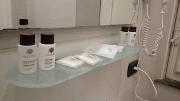 A bathroom with a glass shelf holding toiletries, including body wash and shampoo bottles, and a hairdryer.