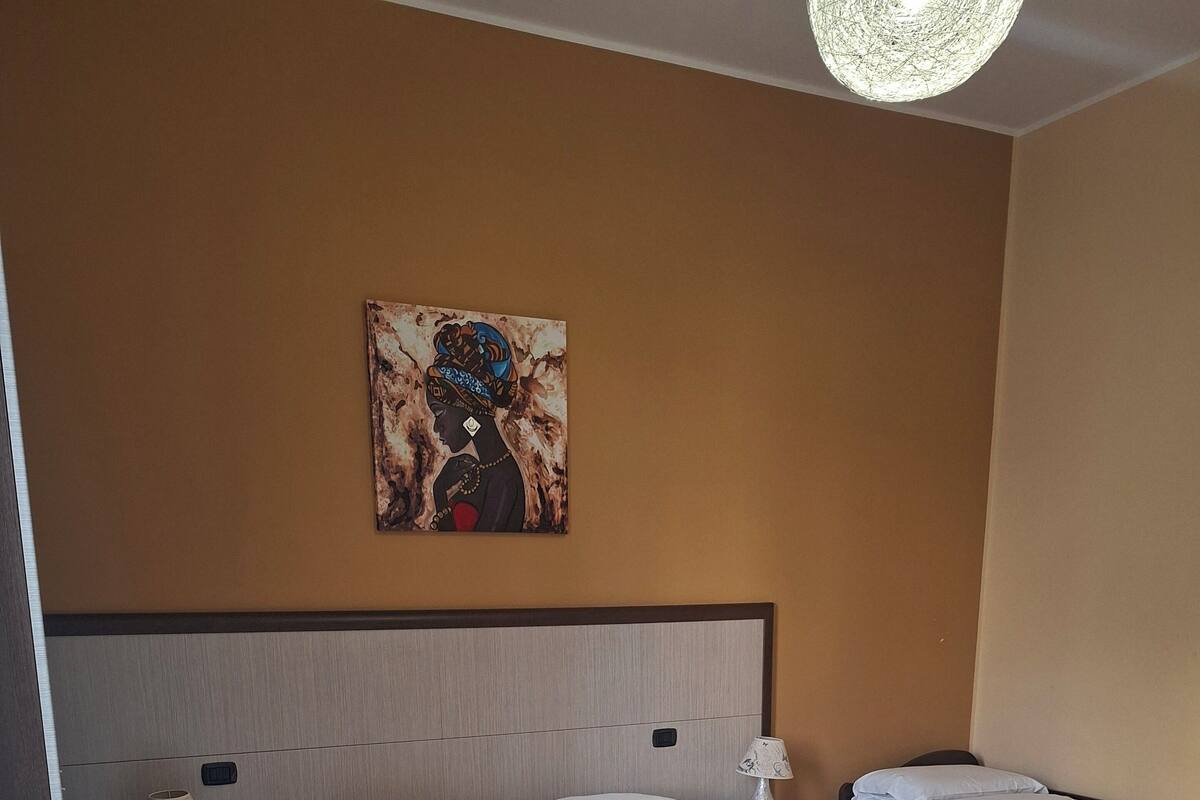 A hotel room with a large bed, a nightstand with a lamp, a bedside table, and a painting on the wall.