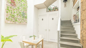 A small patio with a table and chairs, a potted plant, and a staircase leading to an upper level.
