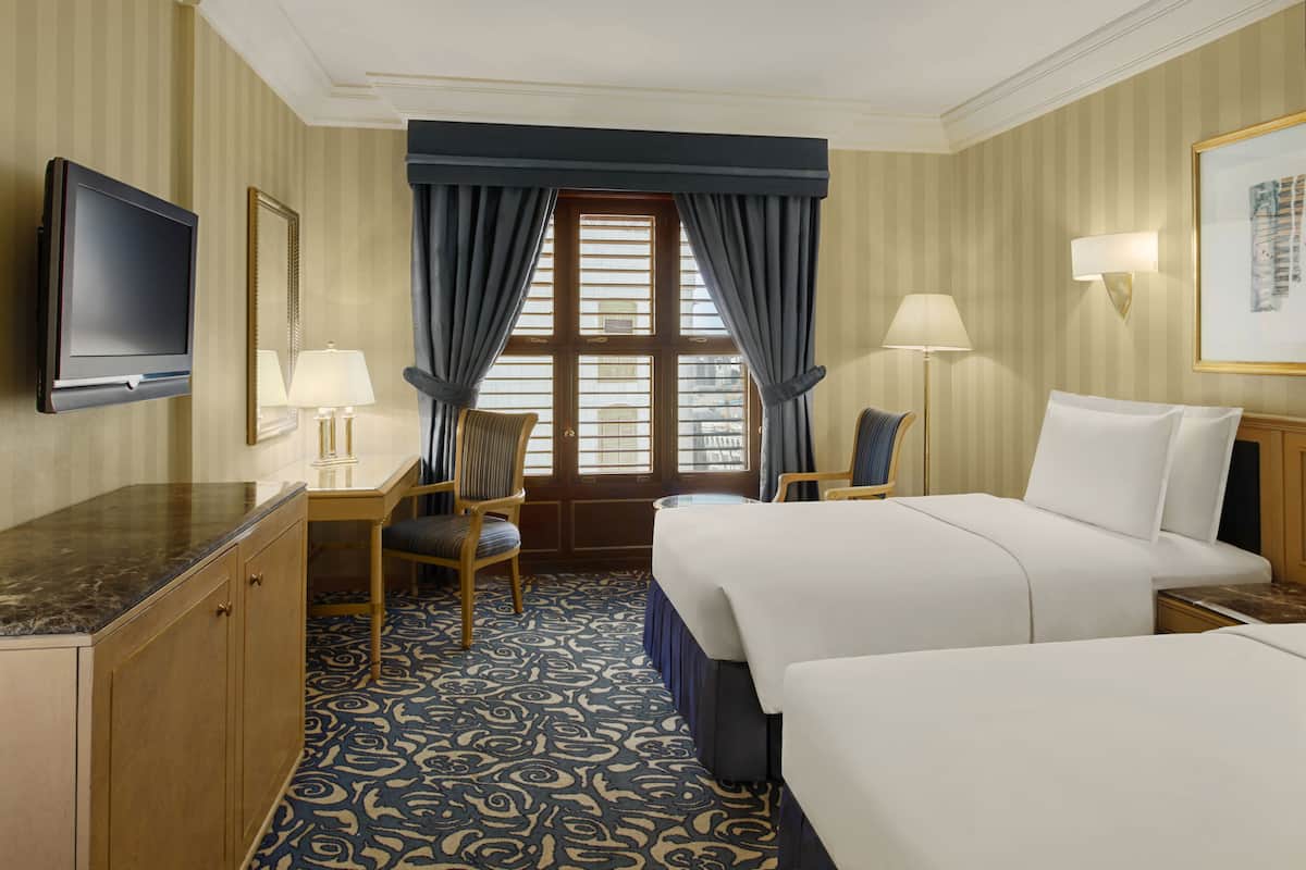 A hotel room with a large bed, a desk with a chair, a television, and a window with curtains.