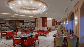 A spacious restaurant with multiple dining areas, a central chandelier, and a kitchen in the background.