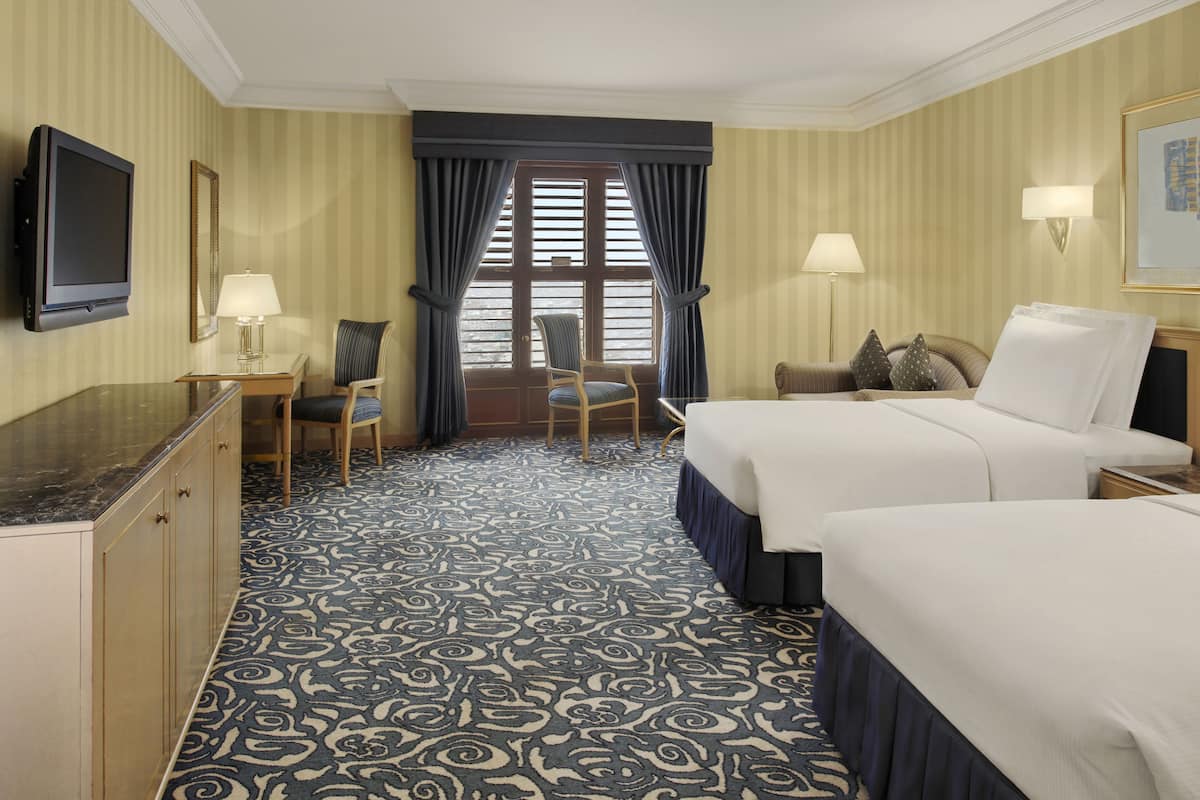 A hotel room with a large bed, a desk with a chair, a television, and a window with curtains.