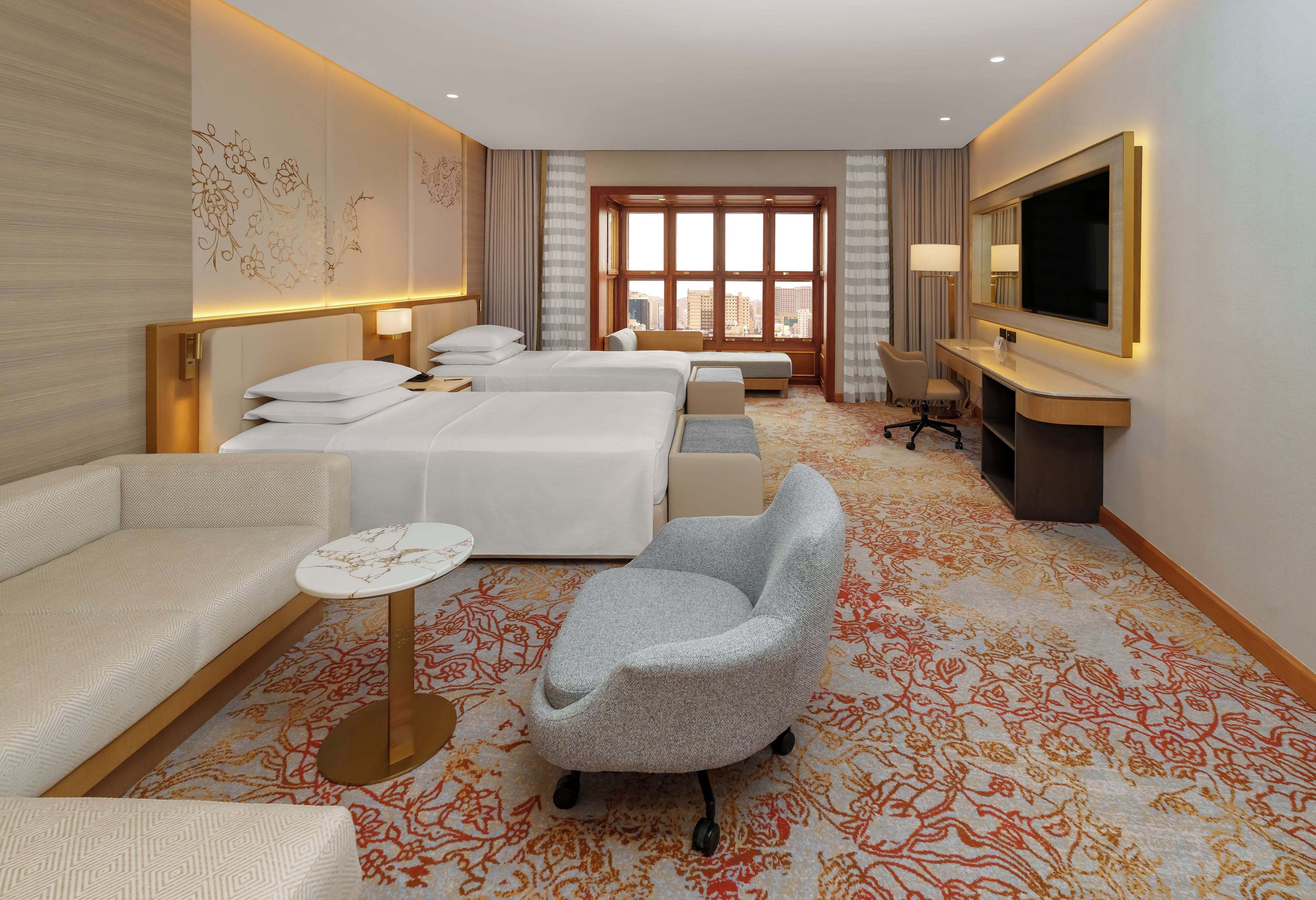 A hotel room with two beds, a sofa, a chair, a desk, and a TV.
