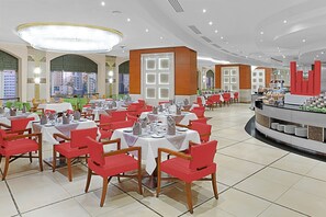 Un amplio comedor con varias mesas y sillas, un mostrador de buffet y grandes ventanales que ofrecen vistas panorámicas de la ciudad.