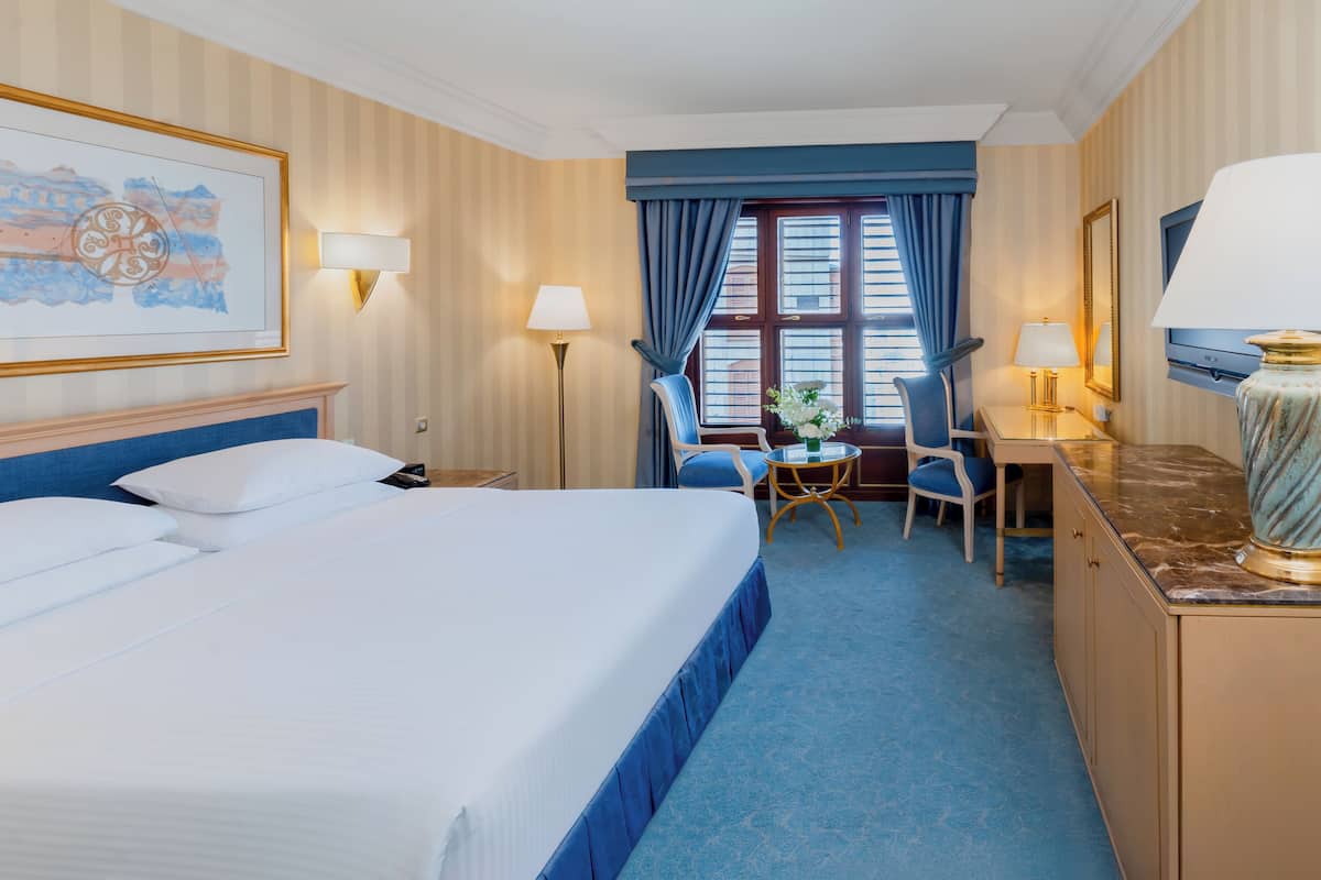 A hotel room with a large bed, a desk, a chair, and a lamp.