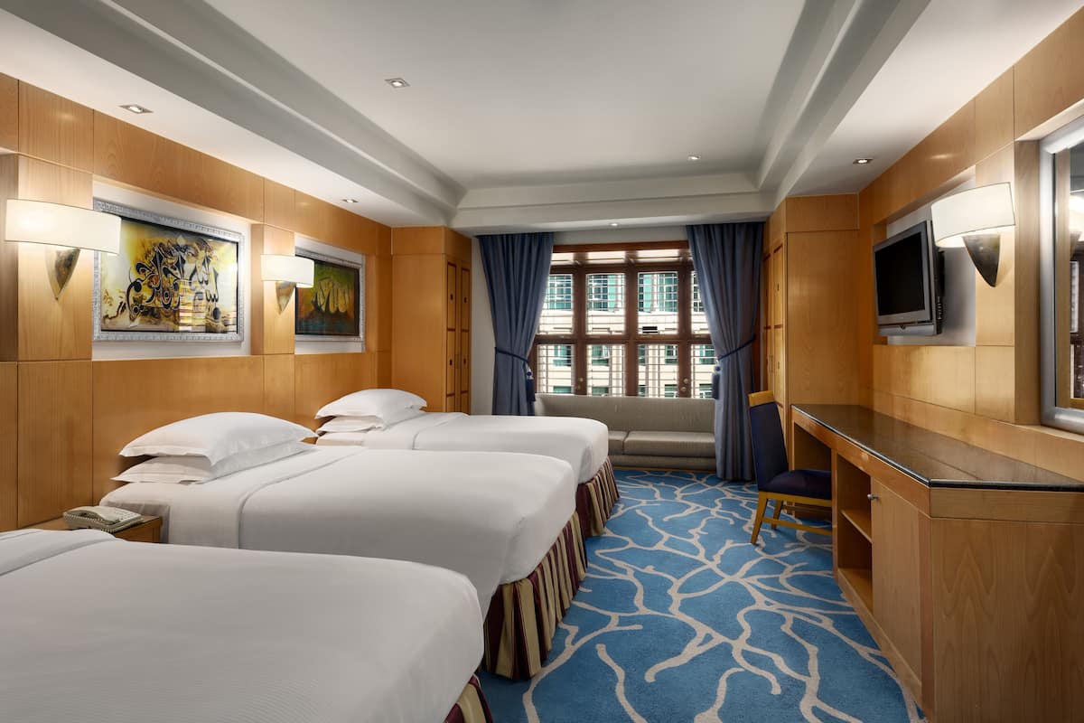 A hotel room with three beds, a desk, a television, and artwork on the walls.