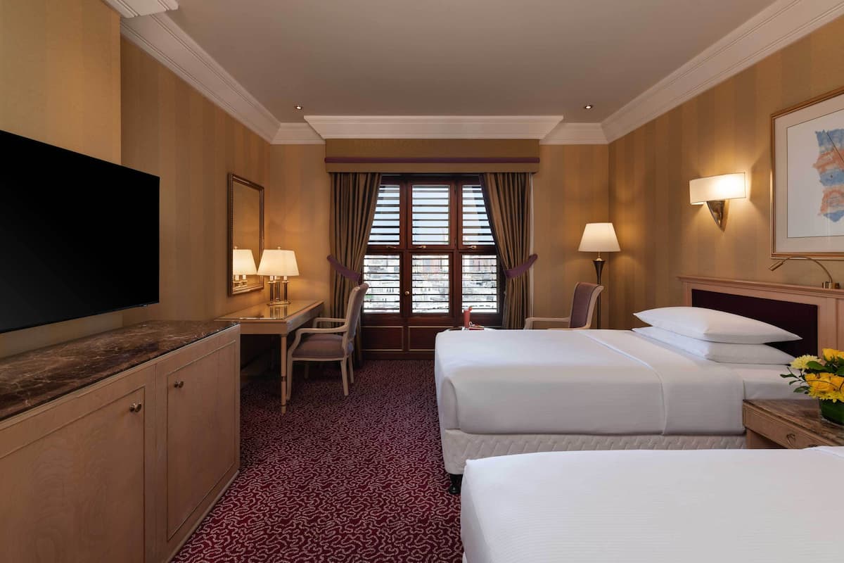 A hotel room with two beds, a desk, a chair, a TV, and a window with curtains.