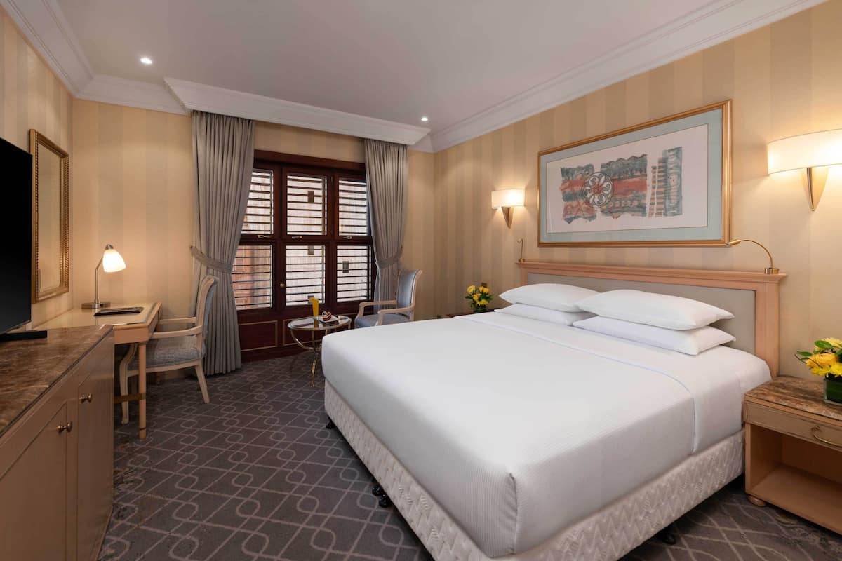A hotel room with a large bed, a desk with a chair, a television, and a window with curtains.