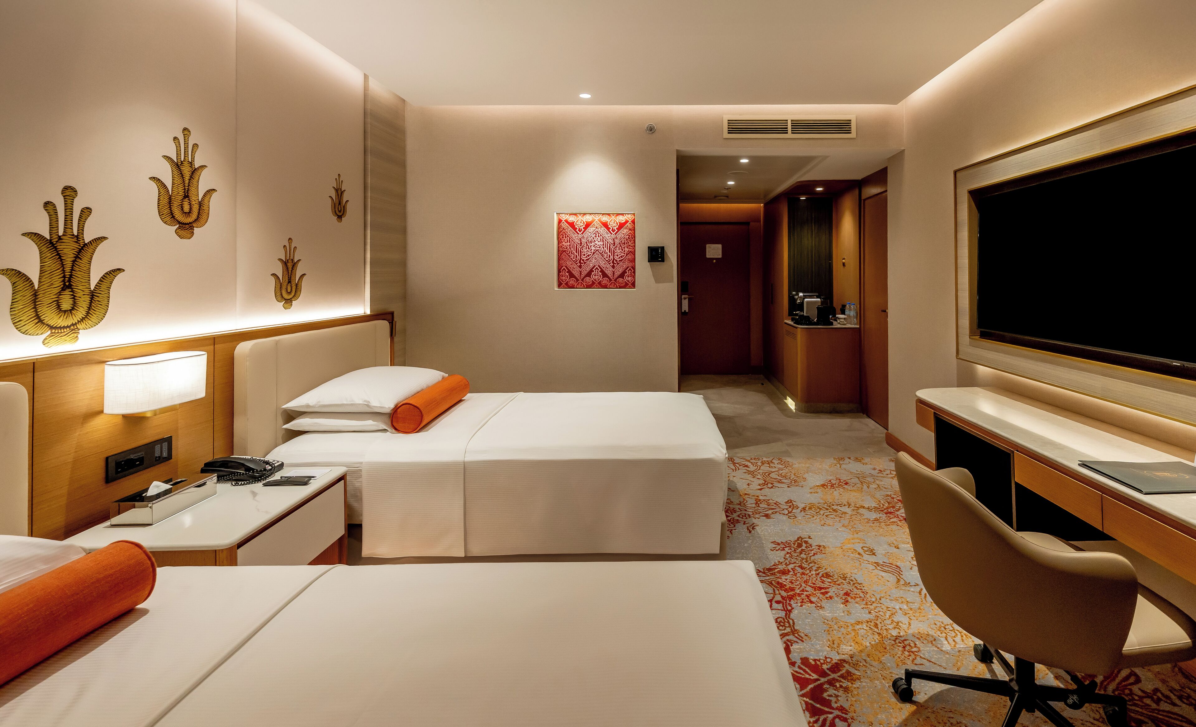 Ein Hotelzimmer mit zwei Betten, einem Schreibtisch, einem Stuhl, einem Fernseher und einem sichtbaren Badezimmer im Hintergrund.