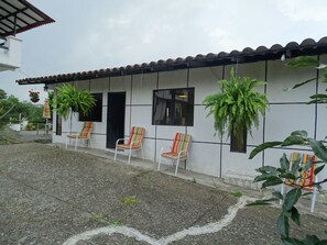 Il s’agit d’un bâtiment doté d’un toit en tuiles et d’une façade blanche. On y voit trois chaises avec des coussins à rayures, placées à l’extérieur.