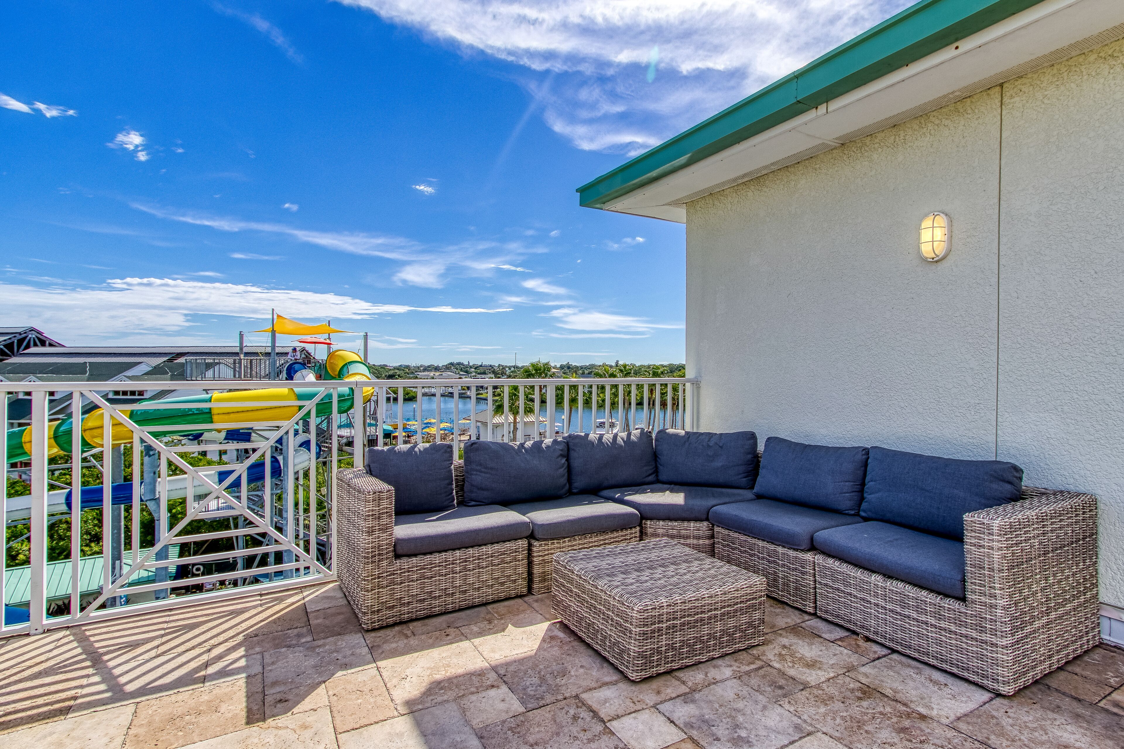 Eine Terrasse mit Korbmöbeln, Blick auf einen Wasserpark und ein Gebäude mit begrüntem Dach.