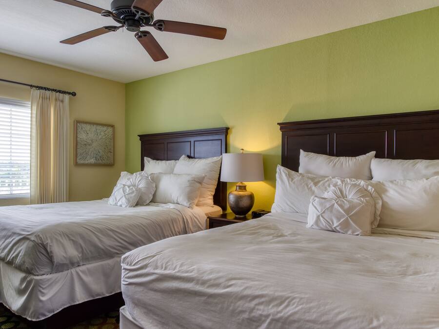 A hotel room with two beds, a ceiling fan, a nightstand with a lamp, and a window with curtains.
