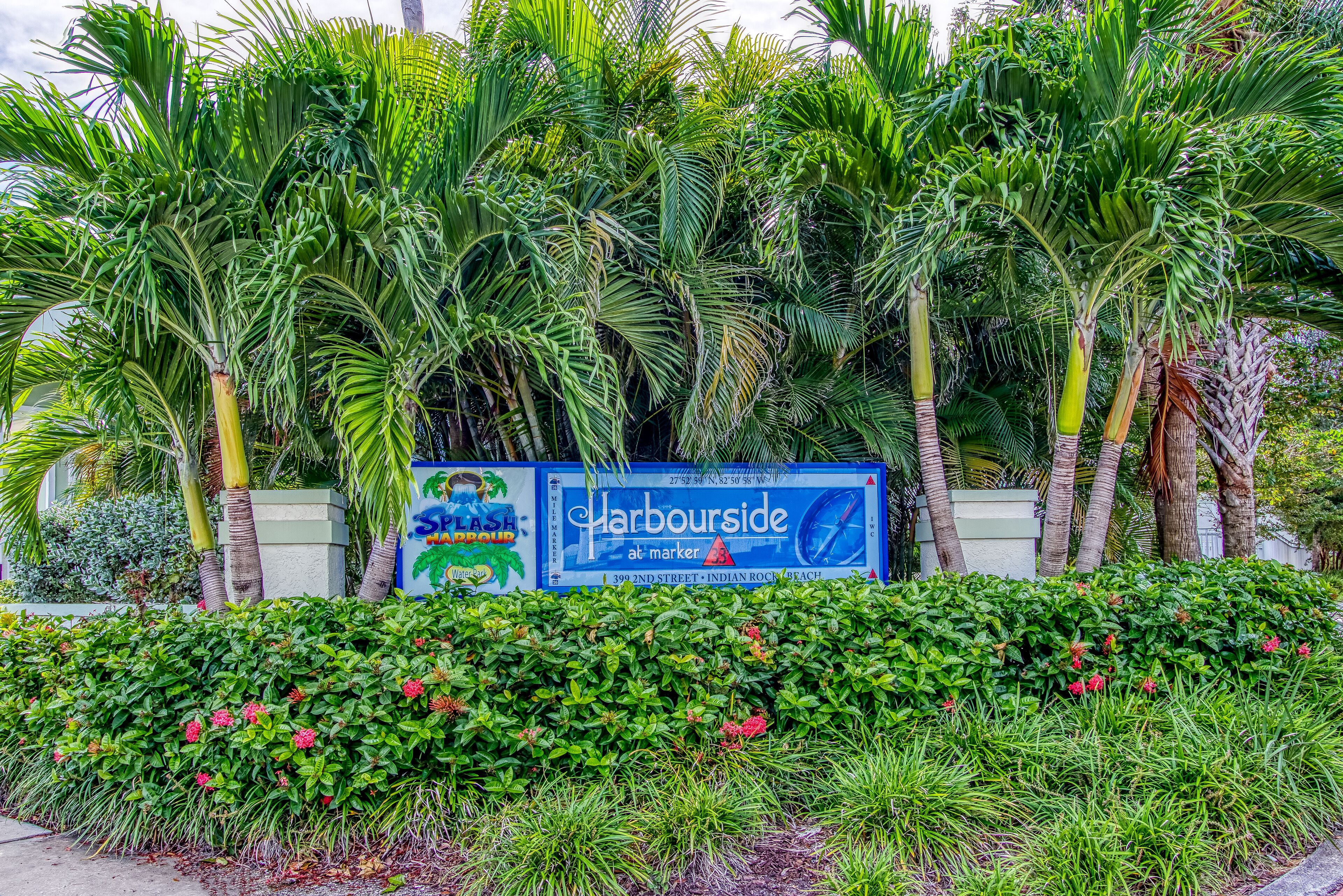 A sign for 'Harbourside at Marker 3' with lush tropical plants and palm trees in the background.