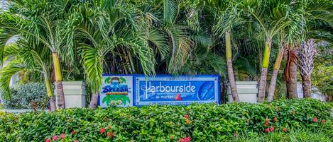 A sign for 'Harbourside at Marker 3' with lush tropical plants and palm trees in the background.