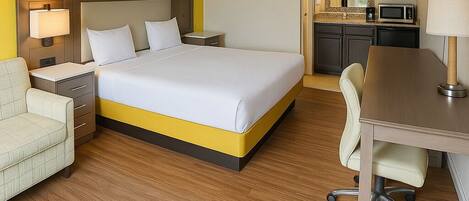 A hotel room with a bed, a desk, a chair, a nightstand, a lamp, a microwave, and a TV.