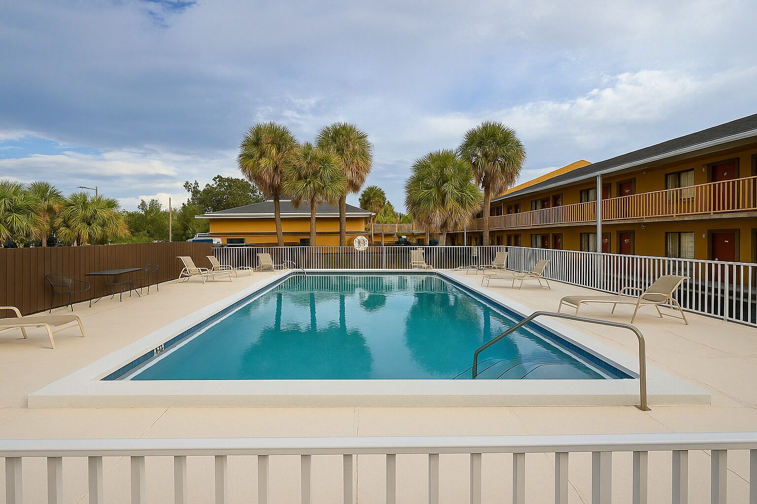 A rectangular pool with a white deck, surrounded by lounge chairs and palm trees.