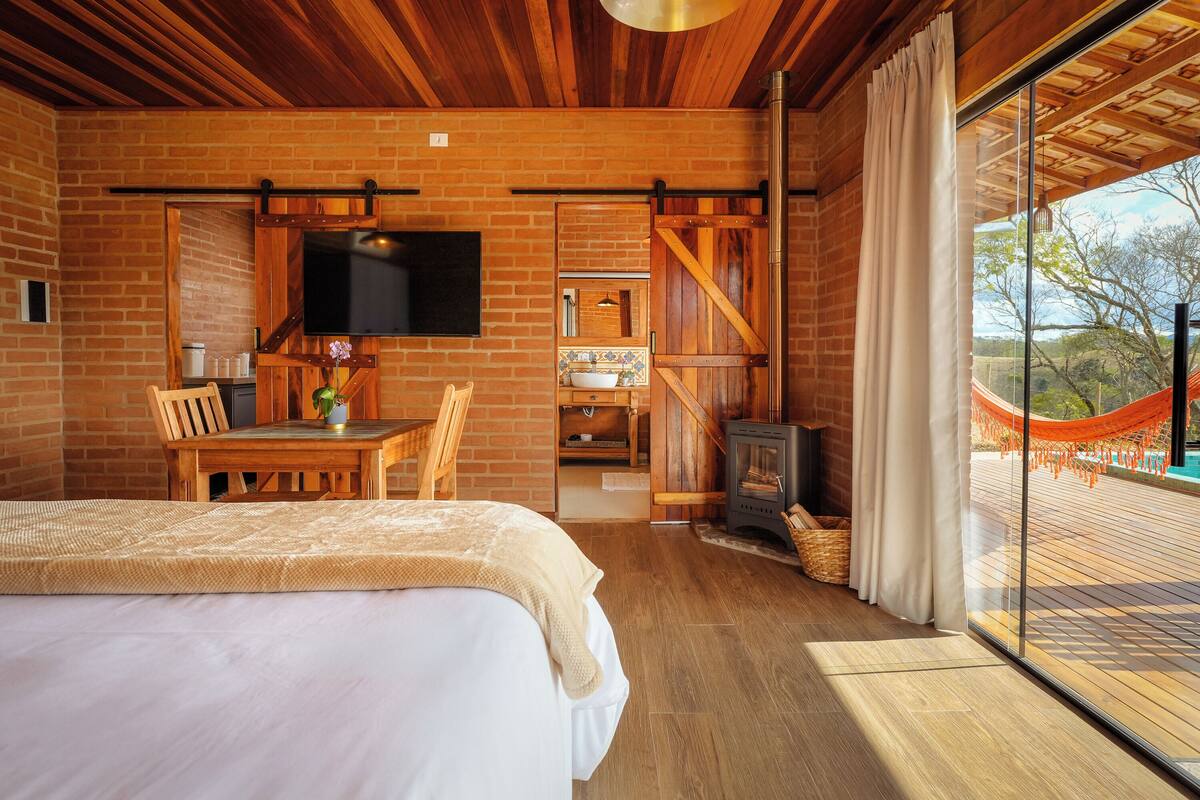 A bedroom with a large bed, wooden furniture, a TV, and a view of a deck with a hammock.