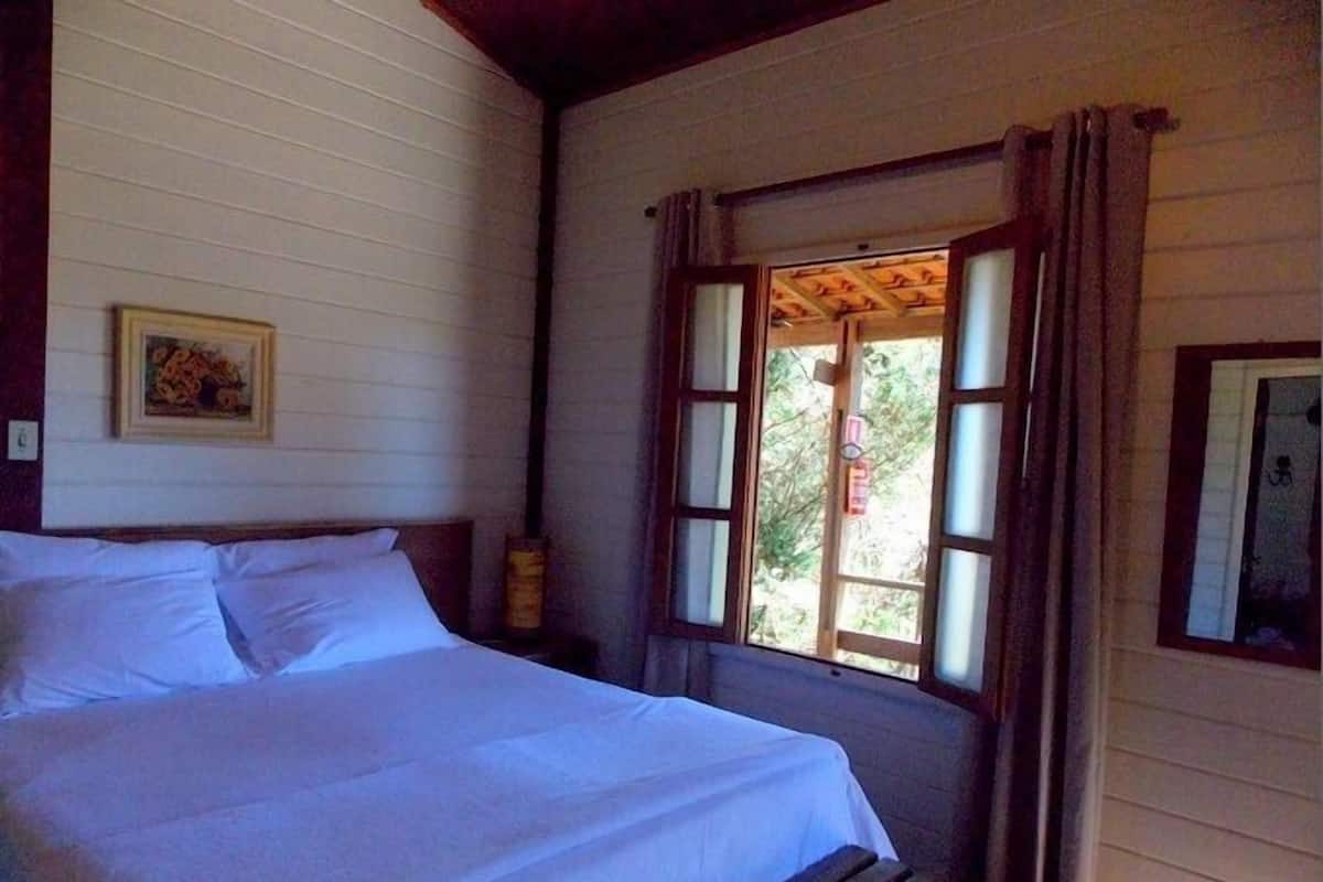 A bedroom with a bed, a window with curtains, a wooden headboard, and a wall-mounted picture.