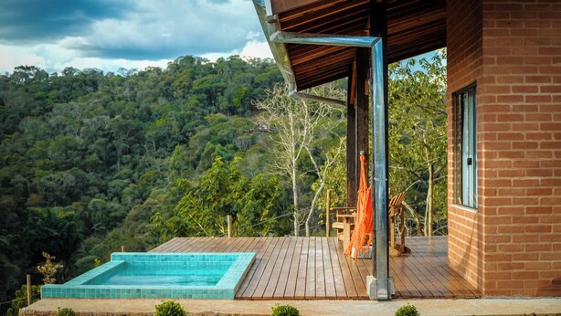 A modern house with a wooden deck, a swimming pool, and a view of a forested hillside. - VELINN Hotel Fazenda Fonte das Hortênsias (Santo Antonio do Pinhal)
