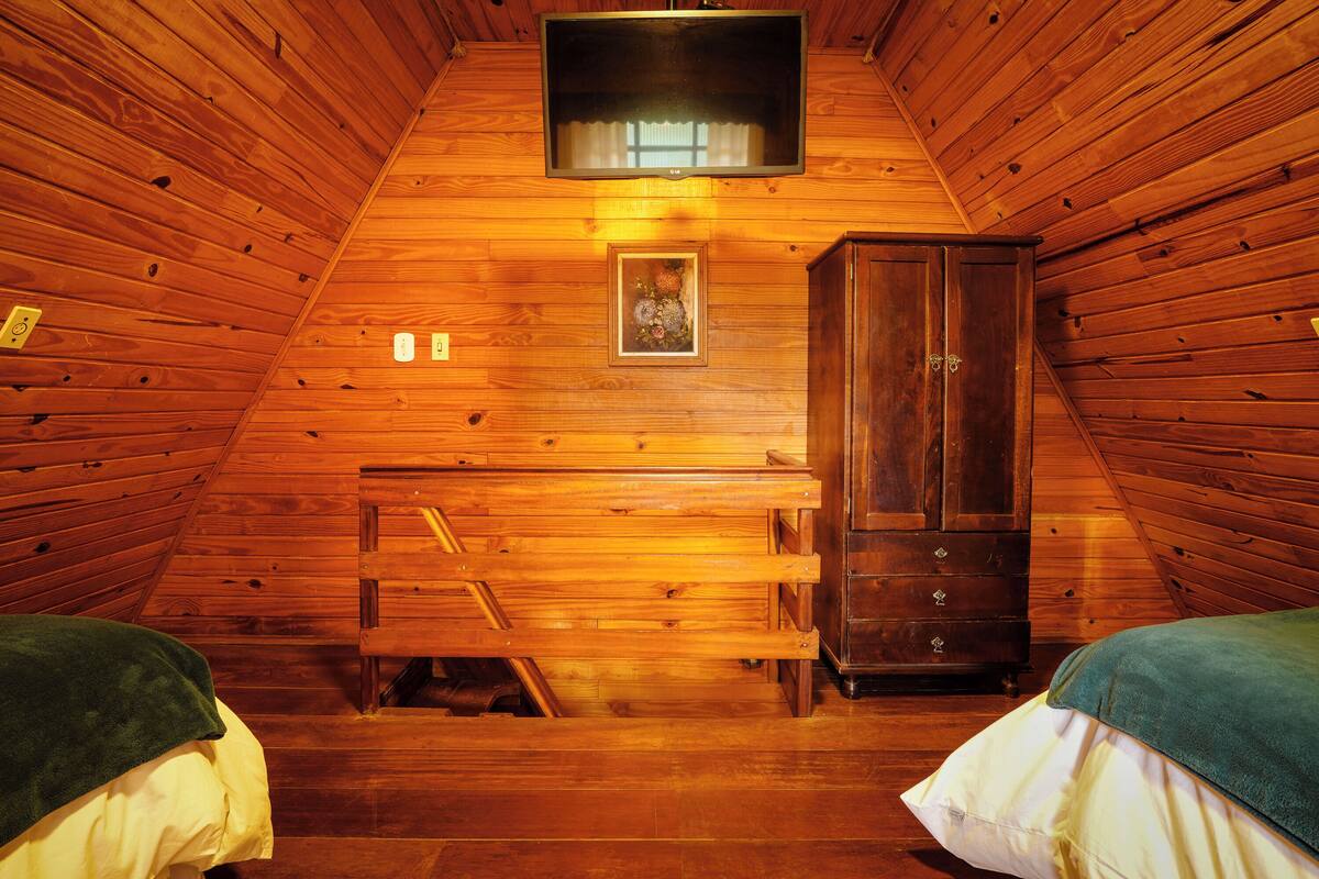 A wooden cabin room with a bed, a cabinet, and a television mounted on the wall.
