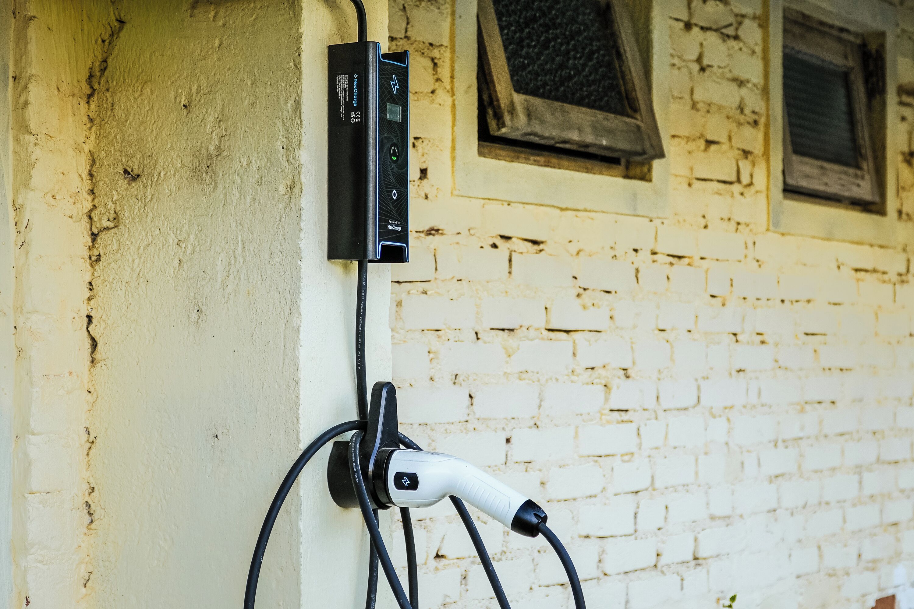 An electric vehicle charging station mounted on a wall with a brick wall background.