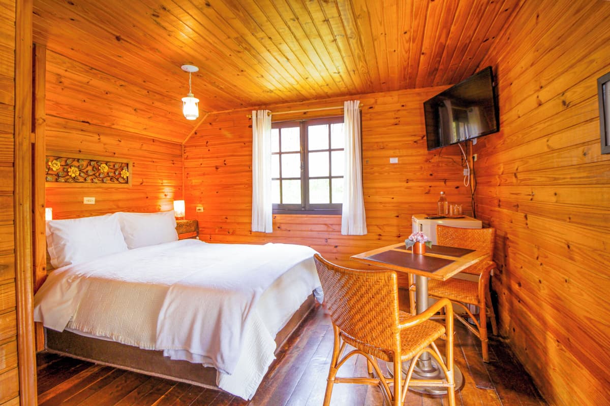 A cozy wooden cabin room with a bed, a desk, and a television.