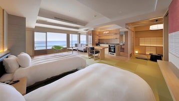 A hotel room with two large beds, a kitchenette, a seating area with a view of the sea, and a separate dining area.