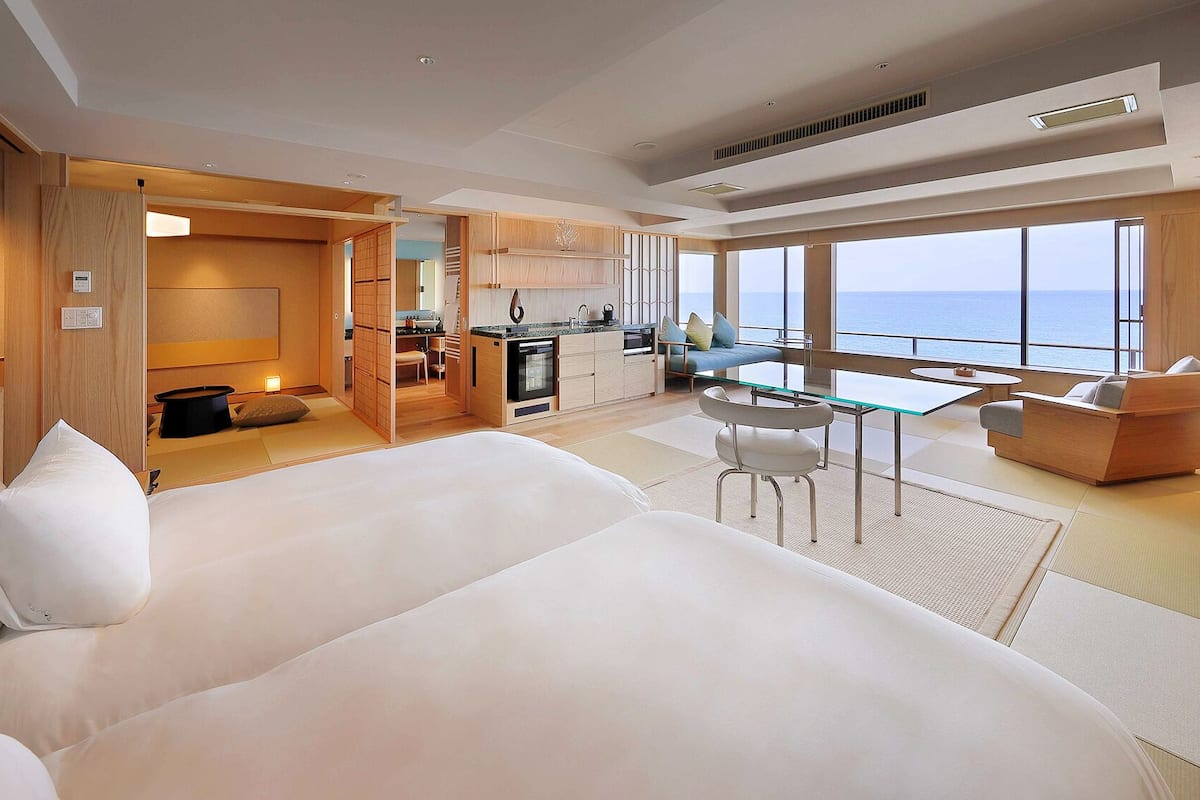 Una habitación de hotel moderna con una cama grande, un área de comedor y vistas al mar.