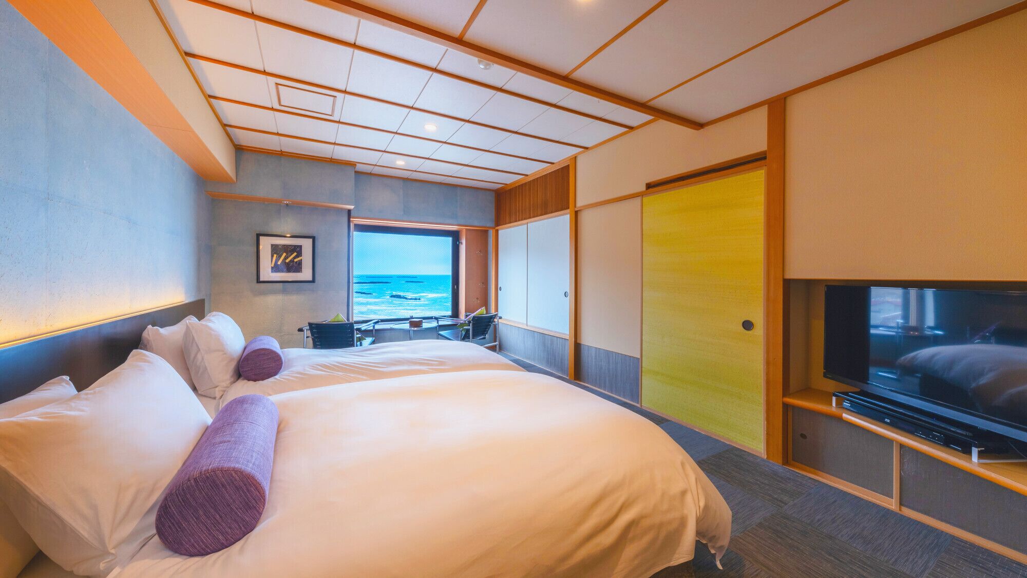 A modern hotel room with a large bed, a TV, and a view of the ocean.