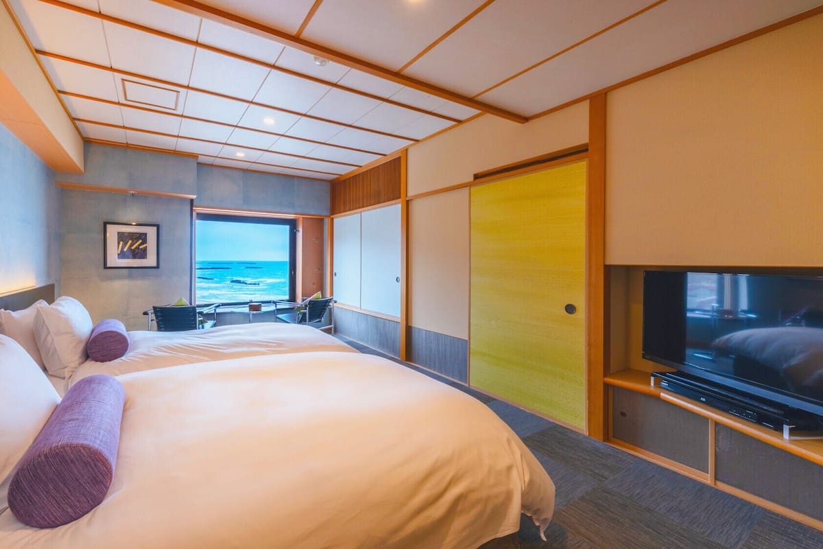 A modern hotel room with a large bed, a TV, and a view of the ocean.