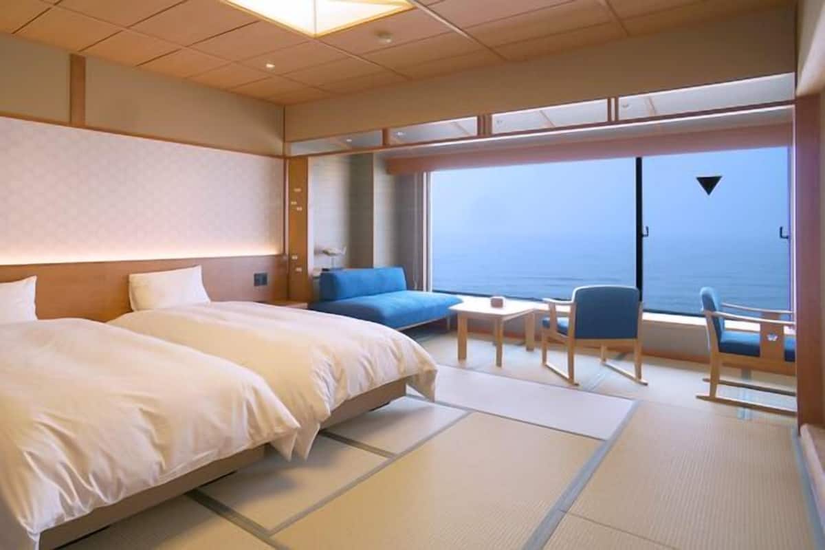 A hotel room with two beds, a small table, a blue sofa, and a view of the sea.