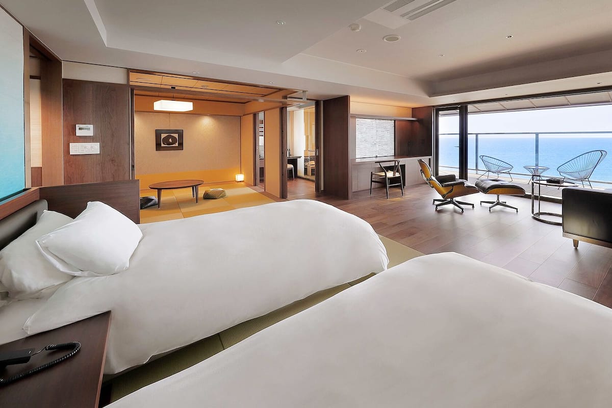 A modern hotel room with a large bed, a desk, a chair, and a view of the ocean.
